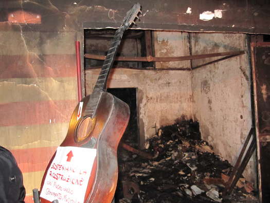 A guitar accepting donations, with the rubble of the Museo dello Strumento Musicale in the background. Photo © 2013 Karen Haid