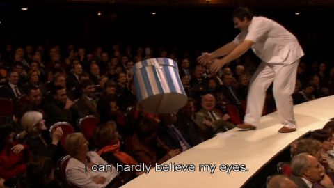 The hat box is passed across the audience to the stage. Screenshot © 2005 Théâtre musical de Paris, Châtelet, and François Roussillon Associés 