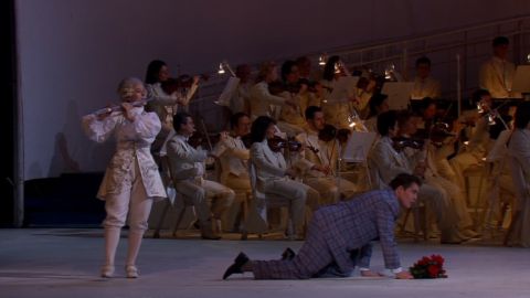 Stage flautist Aglaya Ulanova and Edouard Tsanga as Lord Sidney in front of members of the Mariinsky Theatre Orchestra. Screenshot © 2005 Théâtre musical de Paris, Châtelet, and François Roussillon Associés 